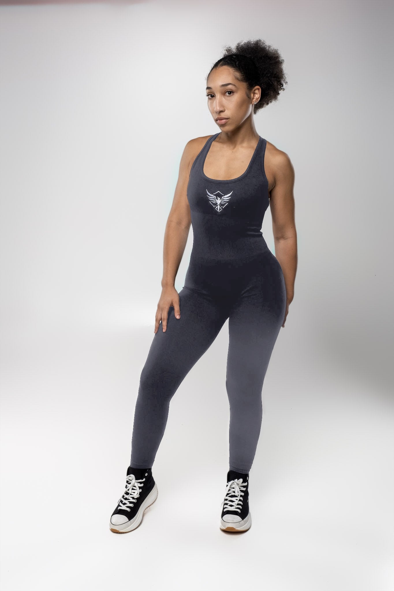 Woman wearing dark gray sleeveless jumpsuit with front logo, sporty activewear fashion outfit